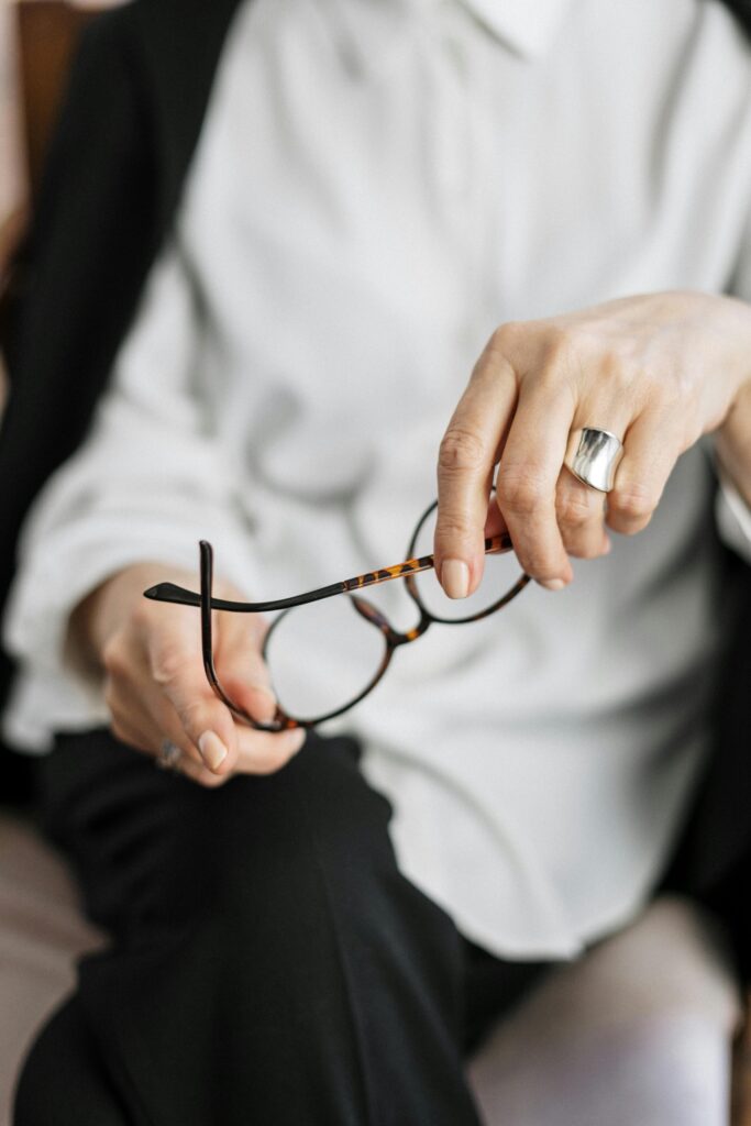 Close-up of a woman’s hand holding glasses, seated in a relaxed posture